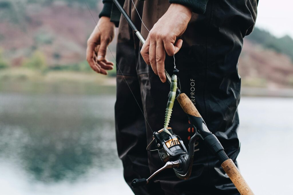 pexels-photo-14339527-14339527 Angler standing by a lake adjusting the fishing rod and bait, ready for a day of fishing.