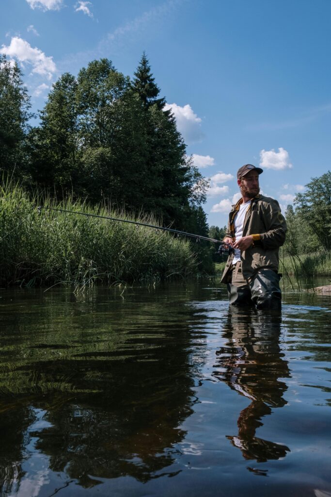 pexels-photo-4828163-4828163 A man enjoys fishing in a tranquil countryside river surrounded by lush greenery and blue skies.